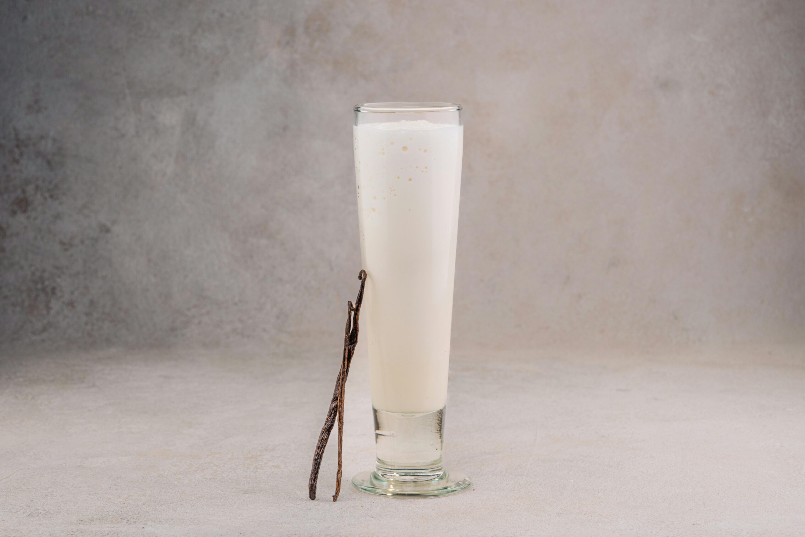 Delicious vanilla-flavored milkshake in a tall glass with a natural beige background, highlighting a fresh vanilla bean garnish.