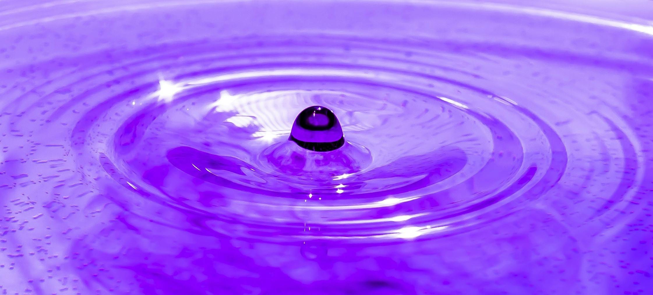 Captivating macro of a droplet creating ripples on a purple liquid surface.
